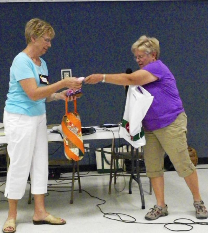 Adie H. presents plastic bag holder  to Silent Auction.