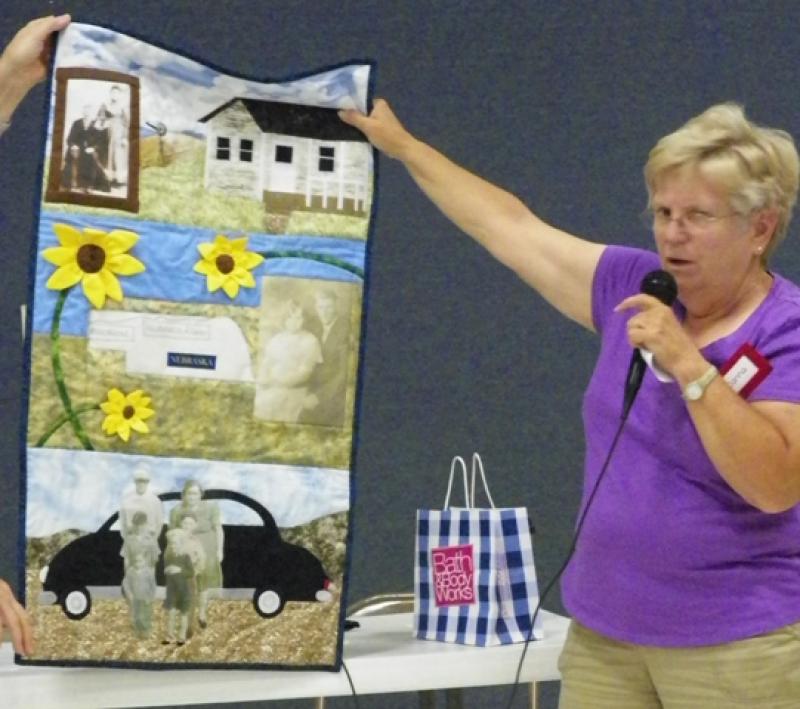 Donna R shows wall hanging picture of grandparents homestead made for Family Reunion.